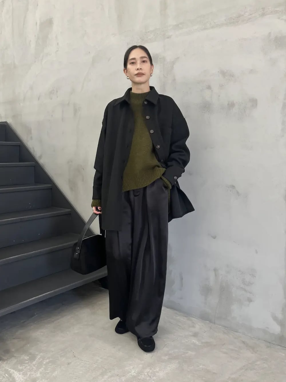 ブラック系のカバーオール、グリーン系のニット/セーター、ブラック系のスラックスを着用したレディースの秋コーディネートの2枚目の写真