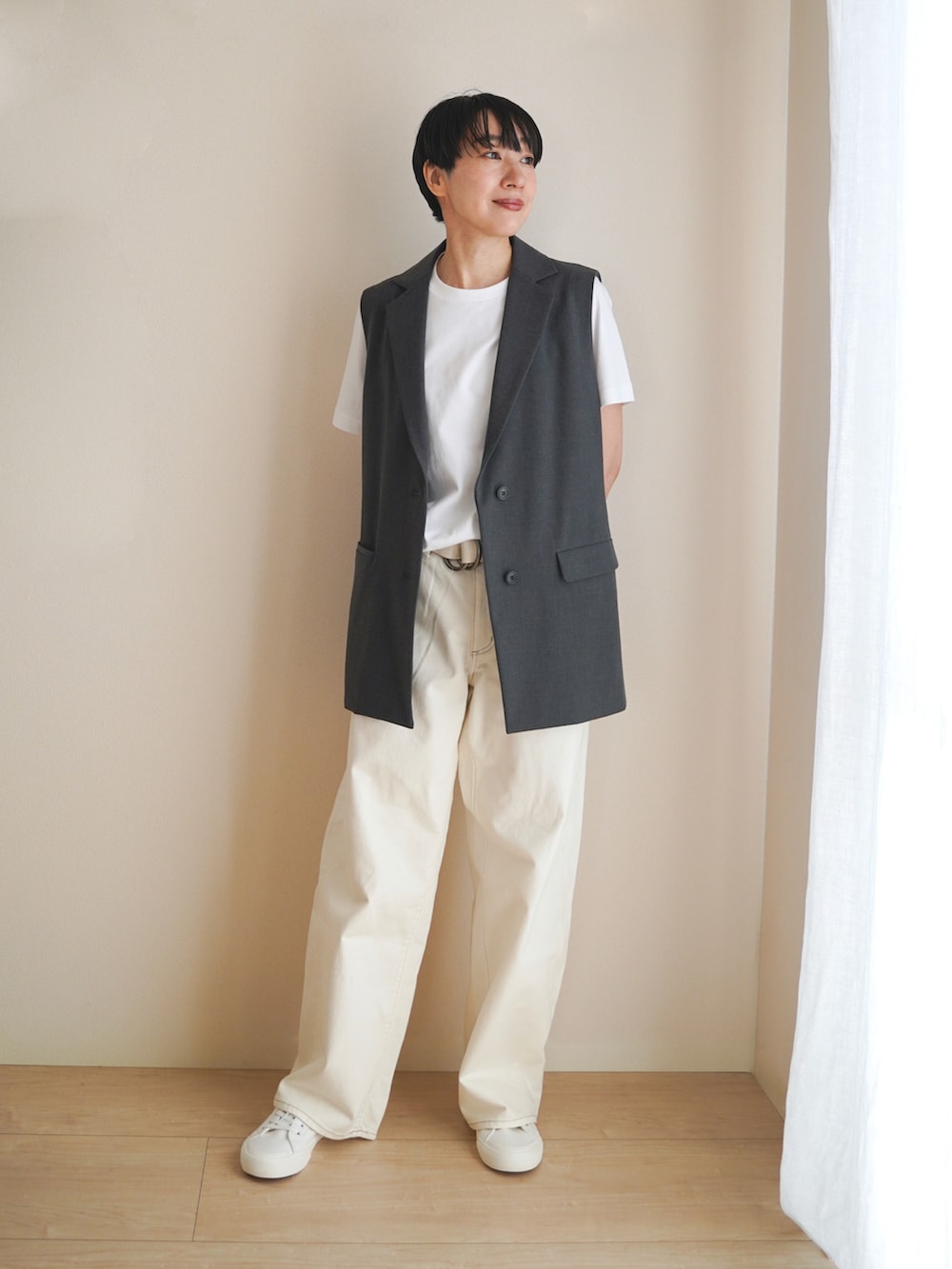 グリーン系のトートバッグ、グレー系のベスト、ホワイト系のデニムパンツを着用したレディースの秋コーディネートの2枚目の写真