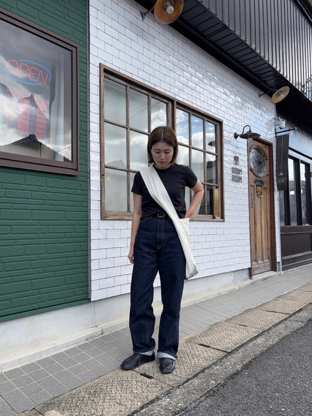 ブルー系のデニムパンツ、ブラック系のモカシン/デッキシューズ、ホワイト系のショルダーバッグを着用したレディースの秋コーディネートの2枚目の写真