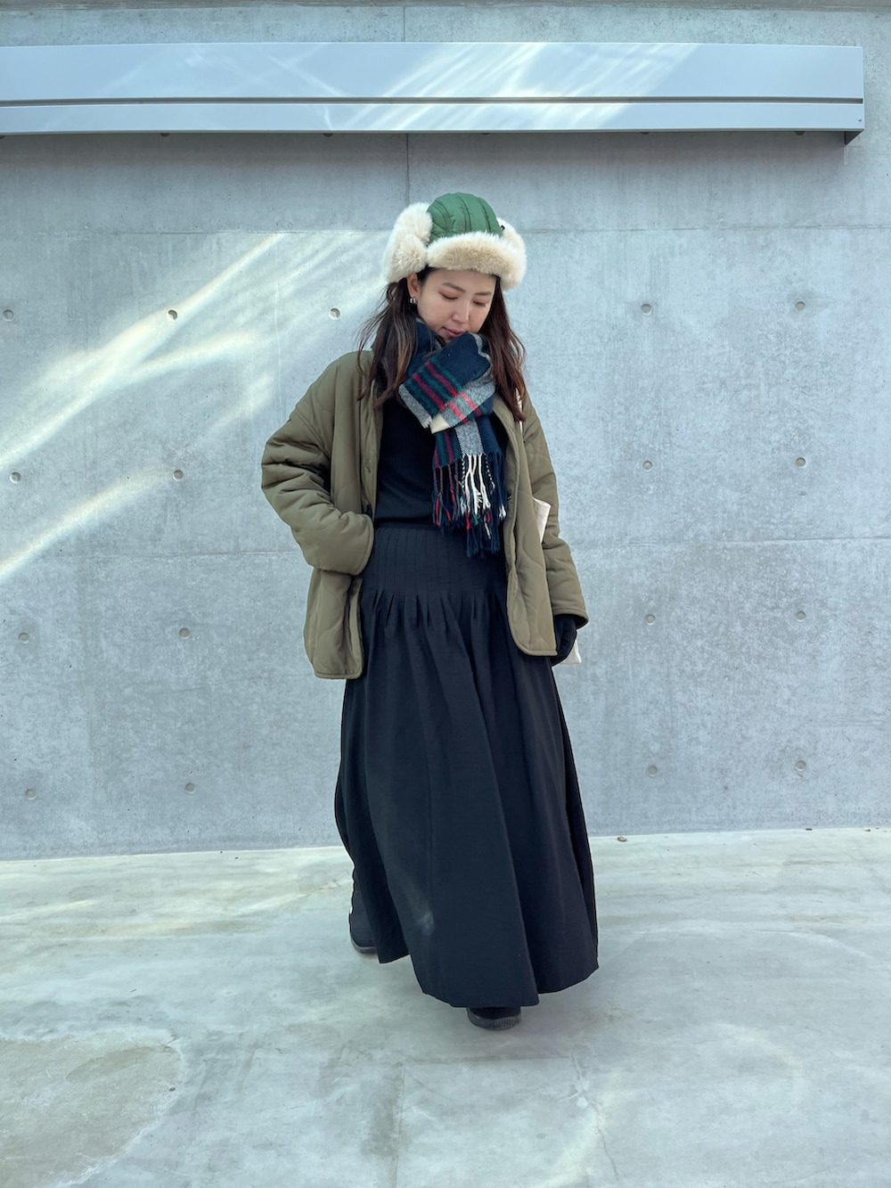 レッド系のトートバッグ、ブラック系のスカート、グリーン系のブルゾンを着用したレディースの冬コーディネートの2枚目の写真
