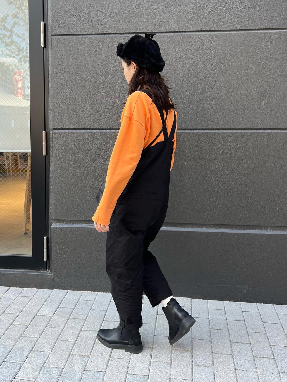 ブラック系のショルダーバッグ、オレンジ系のTシャツ/カットソー、ブラック系のサロペット/オーバーオールを着用したレディースの秋コーディネートの2枚目の写真