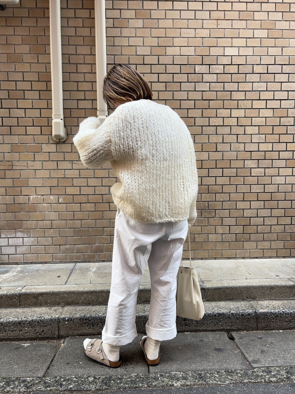 ホワイト系のニット/セーター、ホワイト系のチノパンツ、グレー系のサンダルを着用したレディースの冬コーディネートの2枚目の写真