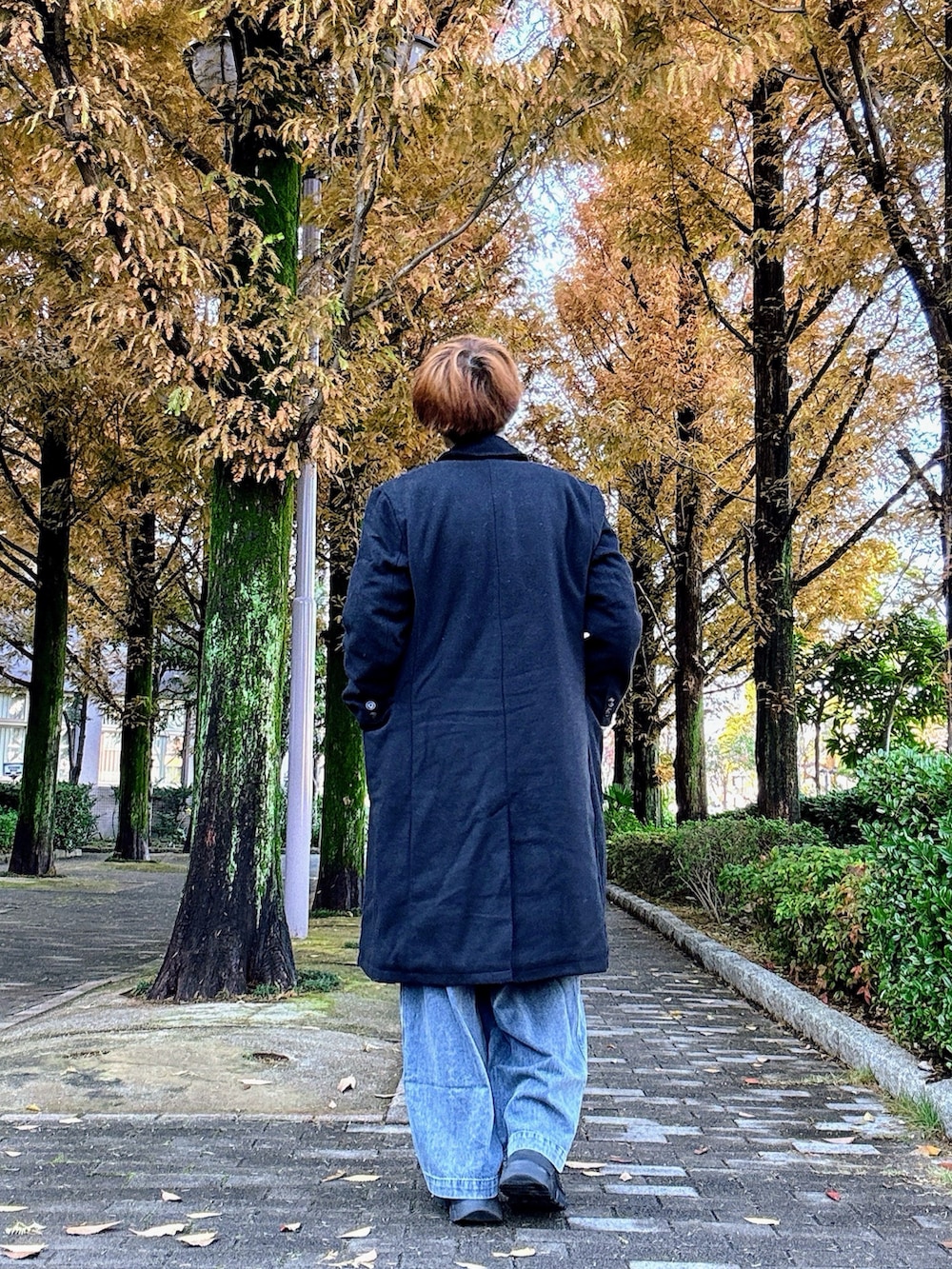 ブラック系のチェスターコート、ホワイト系のスウェット、ブルー系のデニムパンツを着用したメンズの冬コーディネートの2枚目の写真