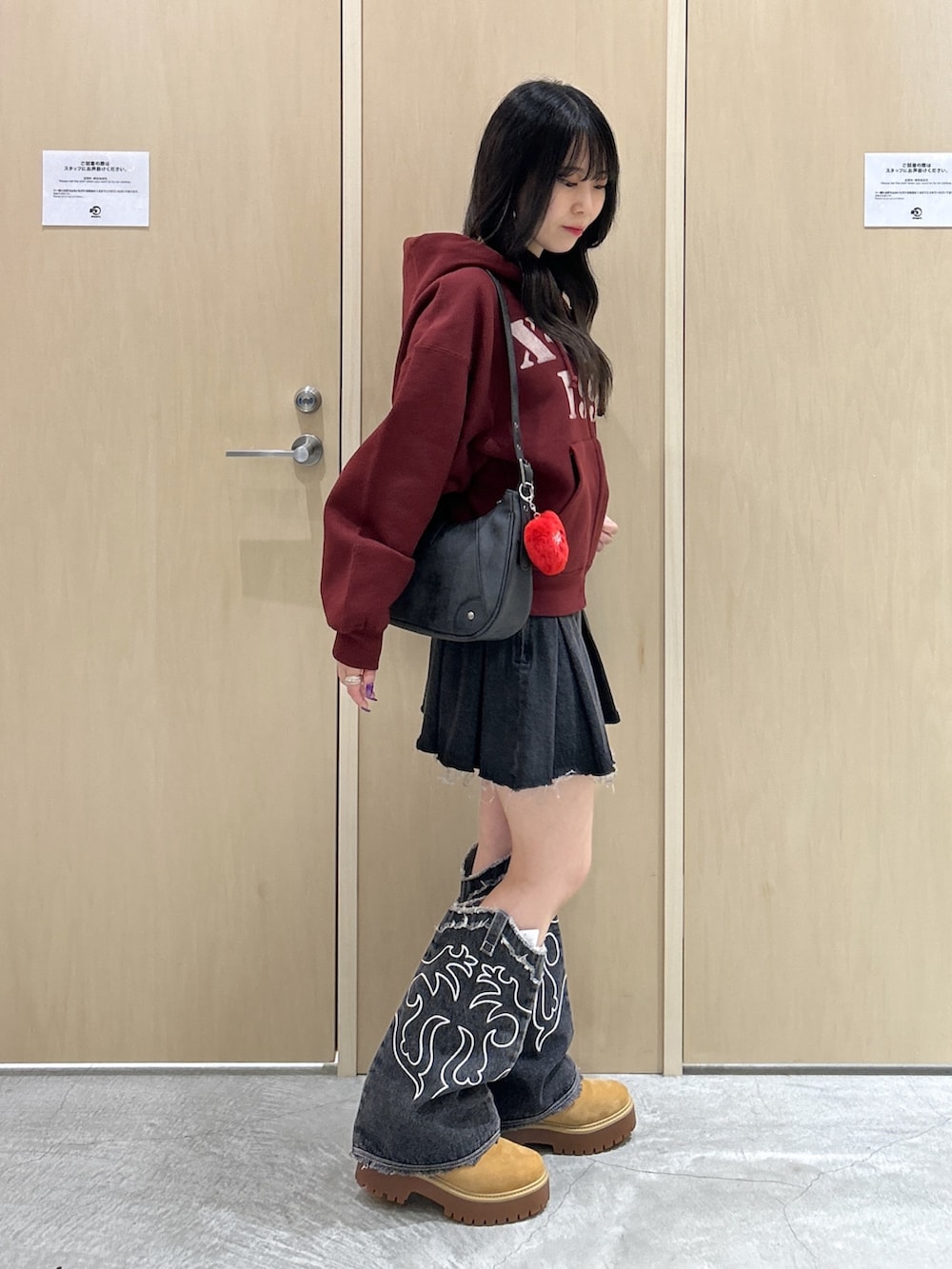 レッド系のパーカー、ブラック系のハンドバッグ、ブラック系のデニムスカートを着用したレディースの秋コーディネートの2枚目の写真