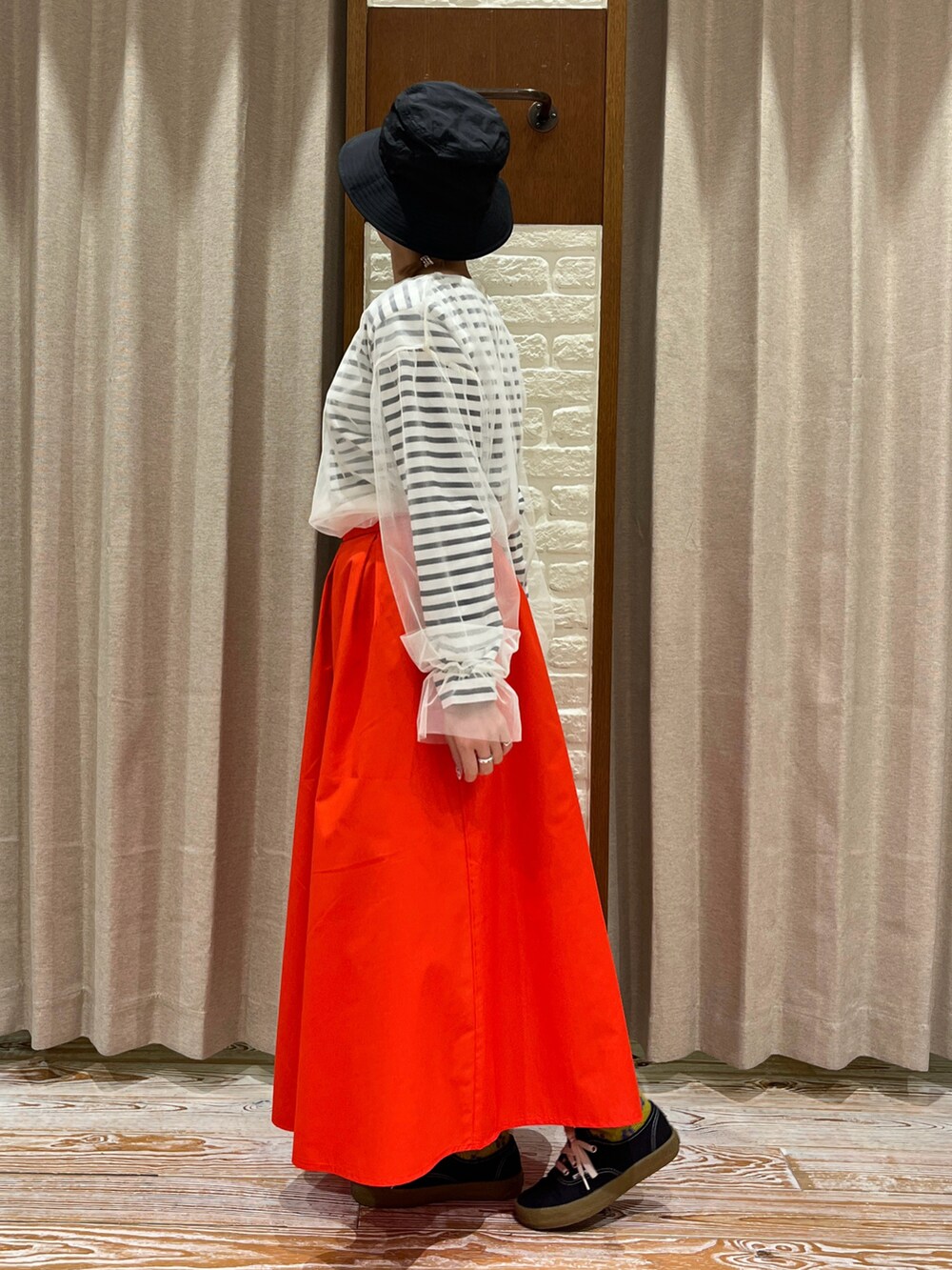 レッド系のスカート、ブラック系のスニーカー、ホワイト系のTシャツ/カットソーを着用したレディースの春コーディネートの2枚目の写真