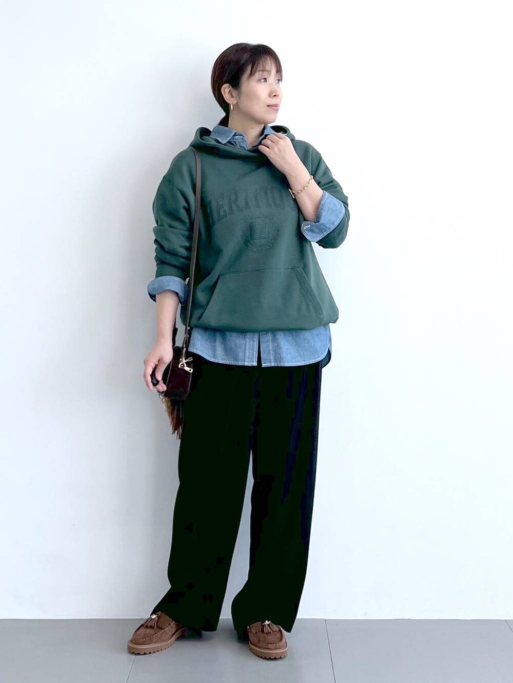 ブラック系のスラックス、グリーン系のパーカー、ブラウン系のショルダーバッグを着用したレディースの秋コーディネートの2枚目の写真