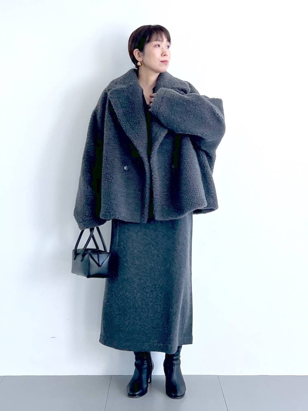 グレー系のピーコート、ブラック系のハンドバッグ、ブラック系のブーツを着用したレディースの秋コーディネートの4枚目の写真