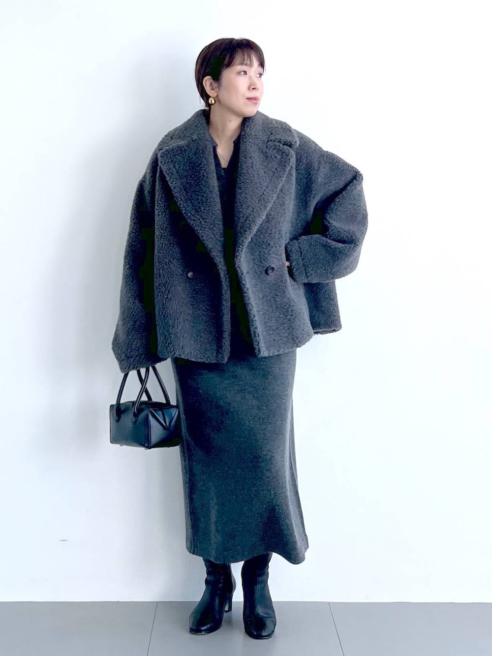 グレー系のピーコート、ブラック系のハンドバッグ、ブラック系のブーツを着用したレディースの秋コーディネートの2枚目の写真