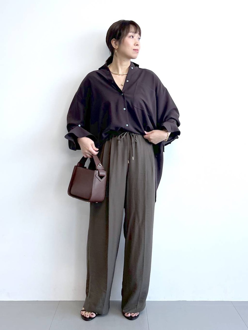 ブラウン系のハンドバッグ、ブラック系のサンダル、ブラウン系のシャツ/ブラウスを着用したレディースの夏コーディネートの2枚目の写真