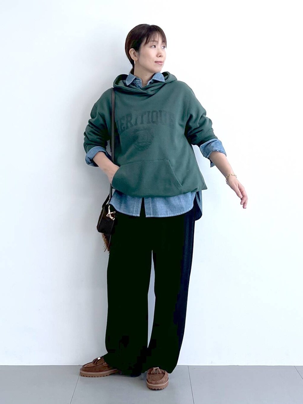 ブラック系のスラックス、グリーン系のパーカー、ブラウン系のショルダーバッグを着用したレディースの秋コーディネートの6枚目の写真