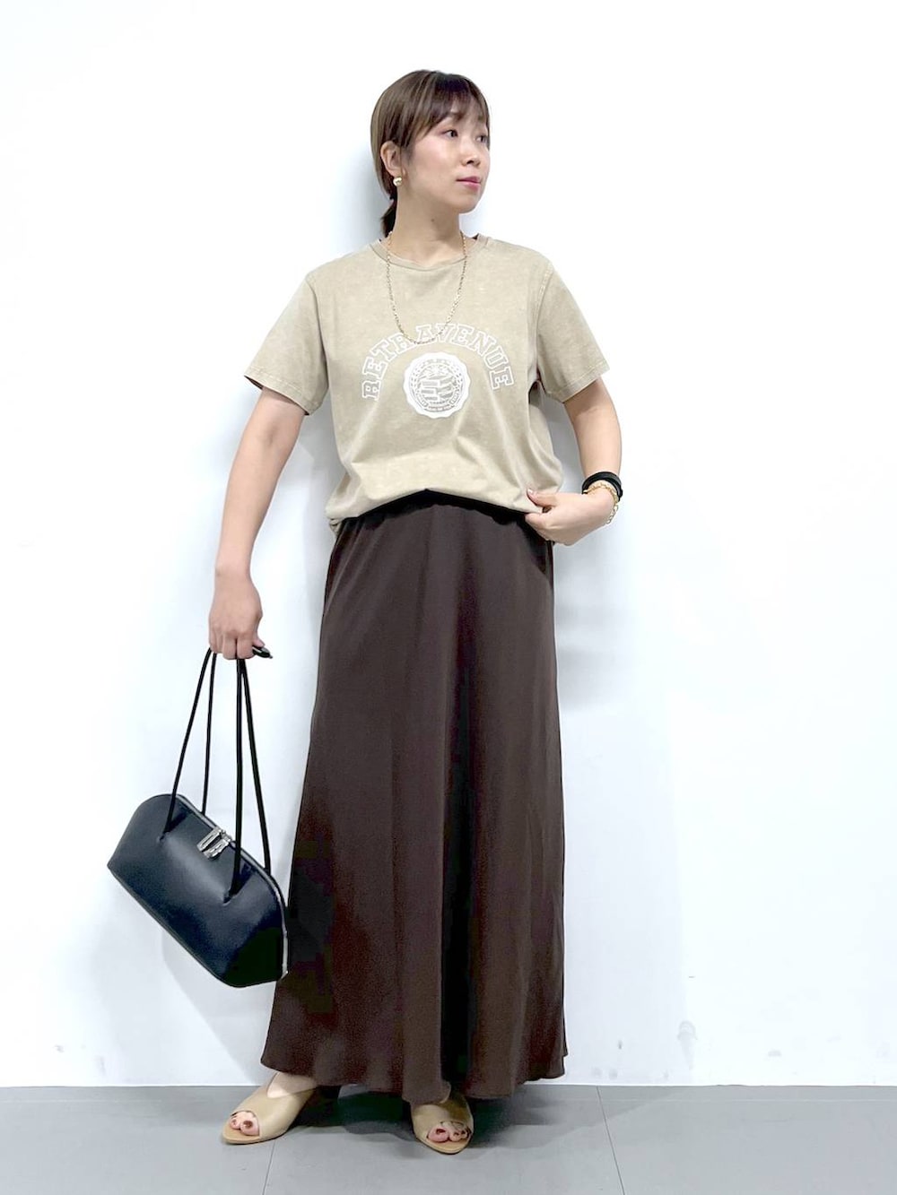 ブラック系のトートバッグ、ベージュ系のサンダル、ベージュ系のTシャツ/カットソーを着用したレディースの夏コーディネートの2枚目の写真