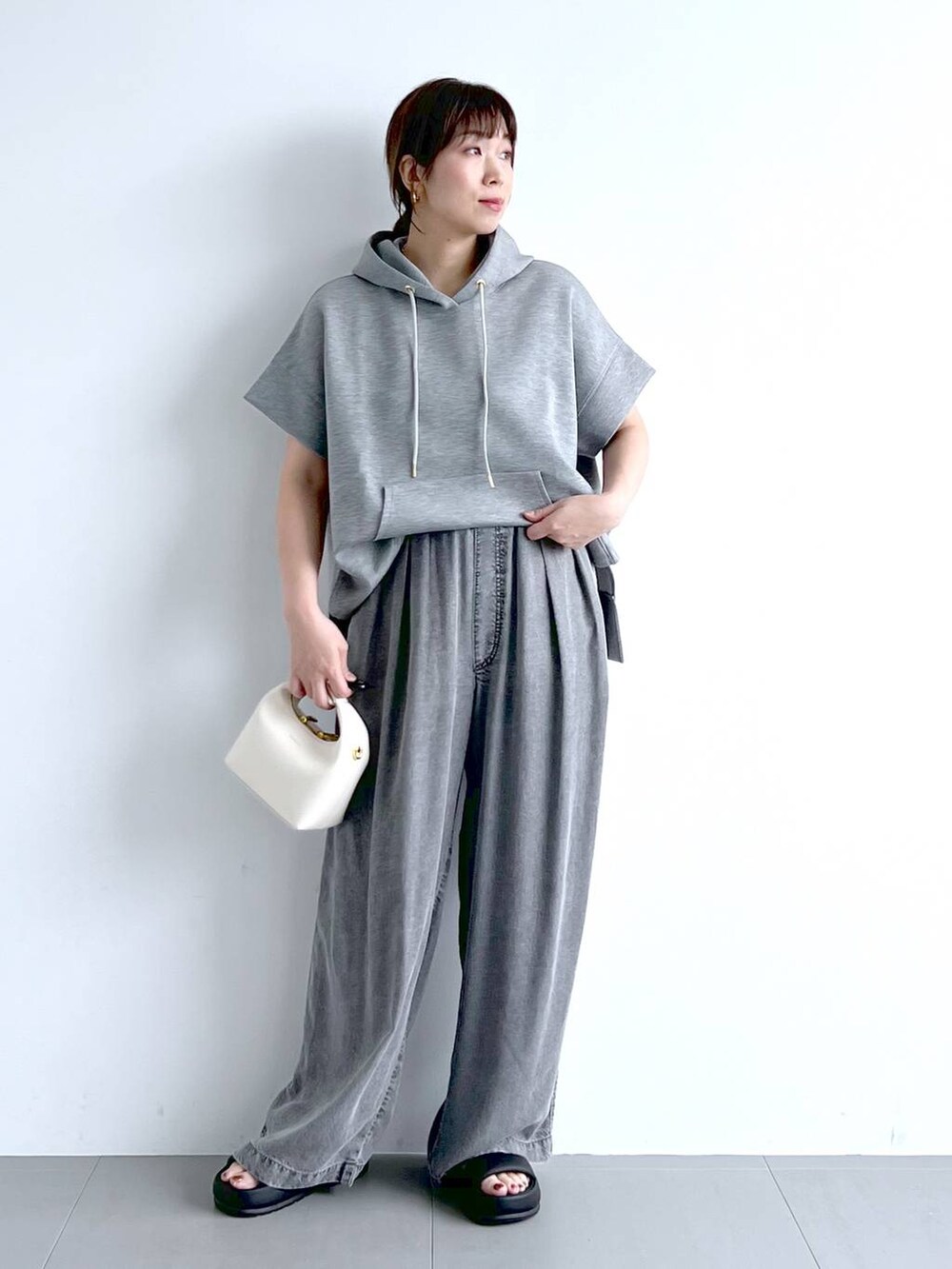グレー系のパーカー、ブラック系のサンダル、ホワイト系のハンドバッグを着用したレディースの夏コーディネートの3枚目の写真