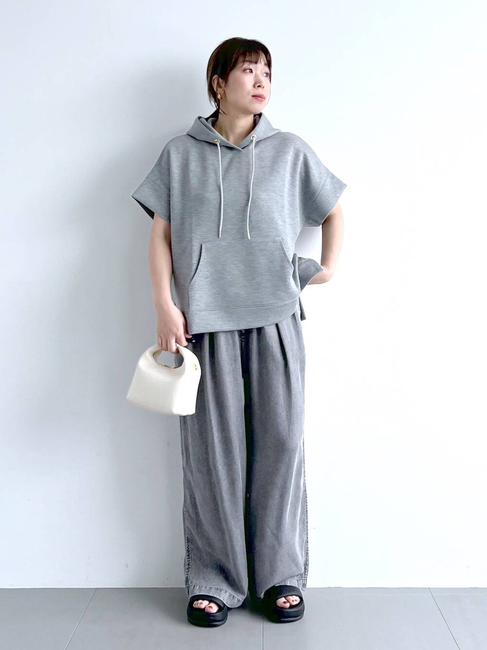 グレー系のパーカー、ブラック系のサンダル、ホワイト系のハンドバッグを着用したレディースの夏コーディネートの6枚目の写真
