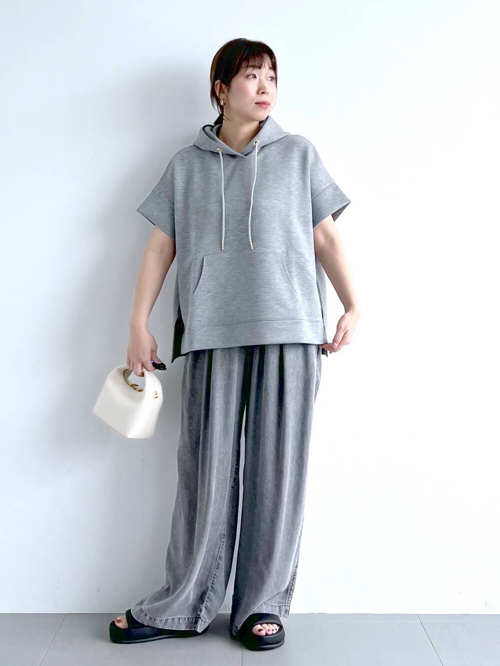 グレー系のパーカー、ブラック系のサンダル、ホワイト系のハンドバッグを着用したレディースの夏コーディネートの2枚目の写真