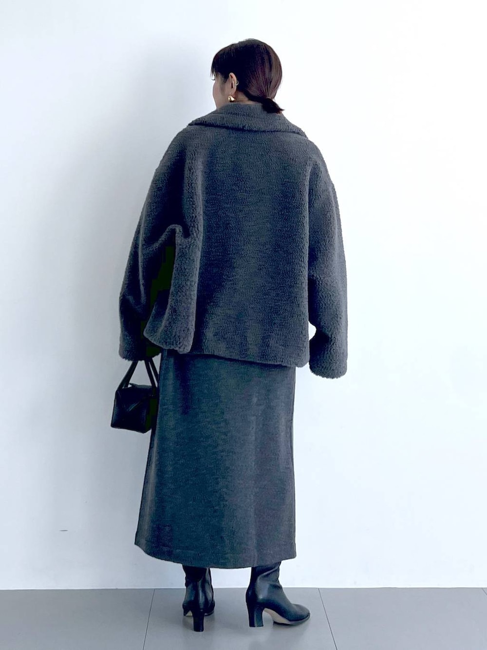 グレー系のピーコート、ブラック系のハンドバッグ、ブラック系のブーツを着用したレディースの秋コーディネートの6枚目の写真