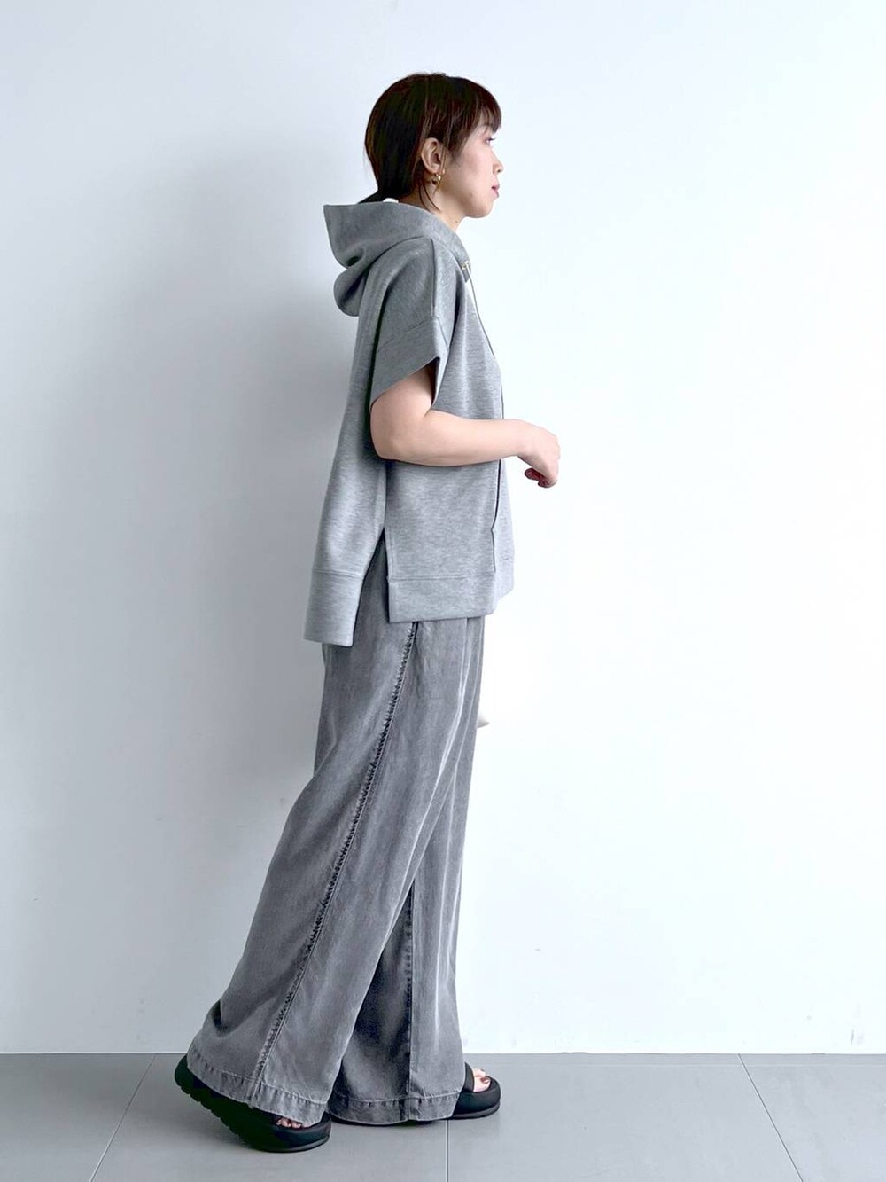 グレー系のパーカー、ブラック系のサンダル、ホワイト系のハンドバッグを着用したレディースの夏コーディネートの7枚目の写真