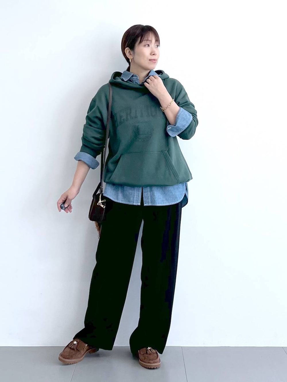 ブラック系のスラックス、グリーン系のパーカー、ブラウン系のショルダーバッグを着用したレディースの秋コーディネートの3枚目の写真