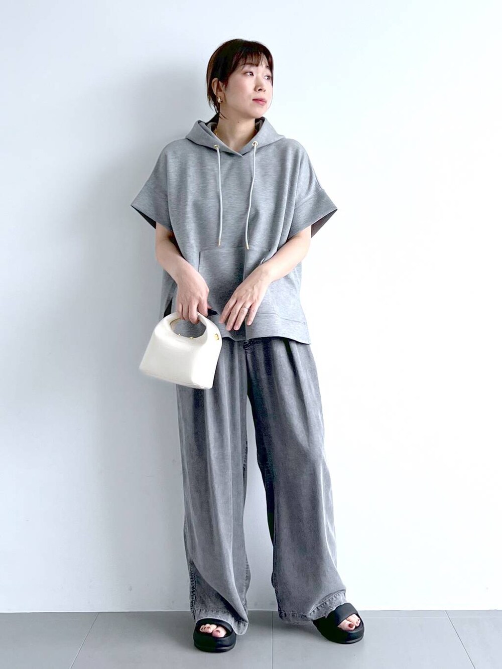 グレー系のパーカー、ブラック系のサンダル、ホワイト系のハンドバッグを着用したレディースの夏コーディネートの4枚目の写真