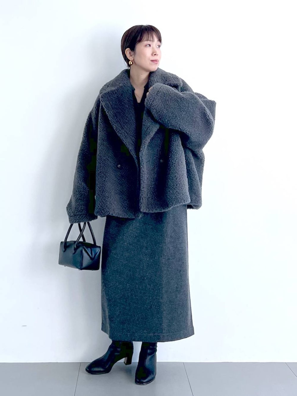 グレー系のピーコート、ブラック系のハンドバッグ、ブラック系のブーツを着用したレディースの秋コーディネートの3枚目の写真