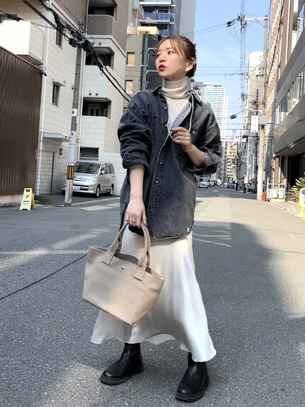 グレー系のトートバッグ、ブラック系のデニムジャケット、ホワイト系のスカートを着用したレディースの春コーディネートの2枚目の写真