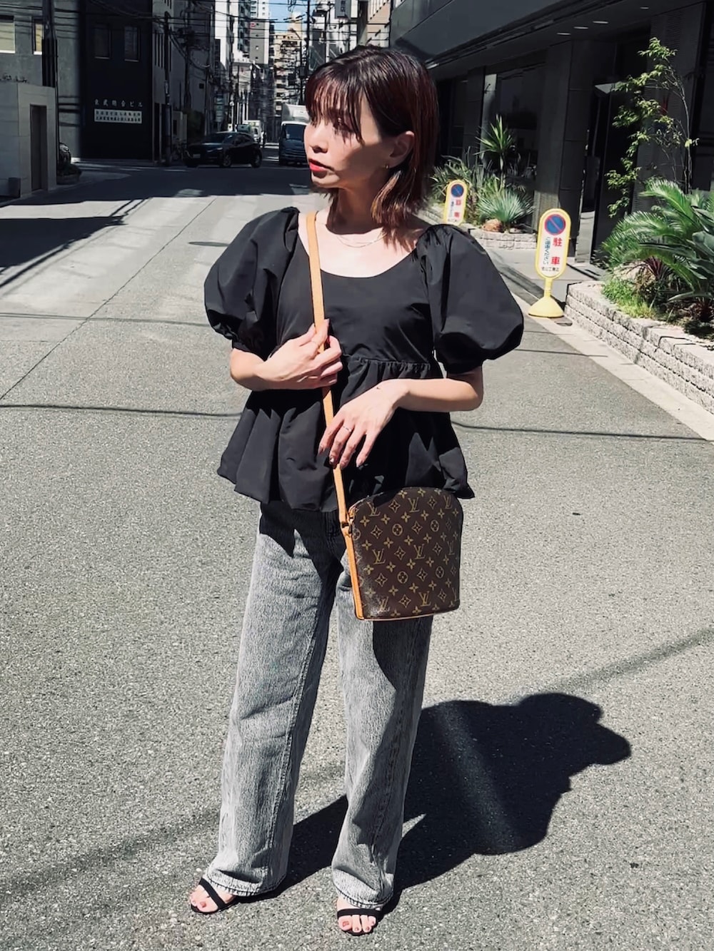 ブラック系のトップス、グレー系のデニムパンツ、ブラウン系のショルダーバッグを着用したレディースの夏コーディネートの4枚目の写真