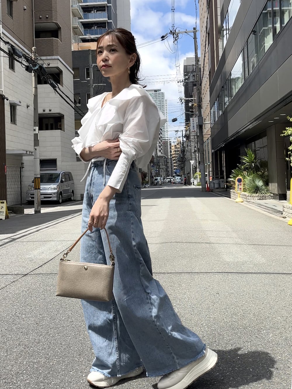 グレー系のショルダーバッグ、ホワイト系のシャツ/ブラウス、グレー系のデニムパンツを着用したレディースの春コーディネートの2枚目の写真