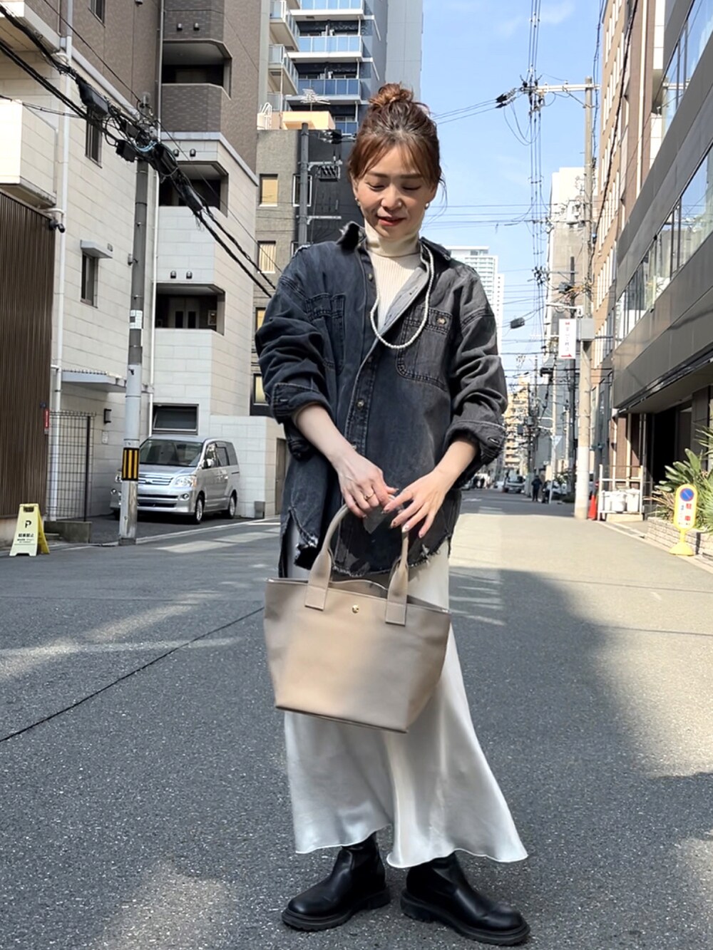 グレー系のトートバッグ、ブラック系のデニムジャケット、ホワイト系のスカートを着用したレディースの春コーディネートの4枚目の写真