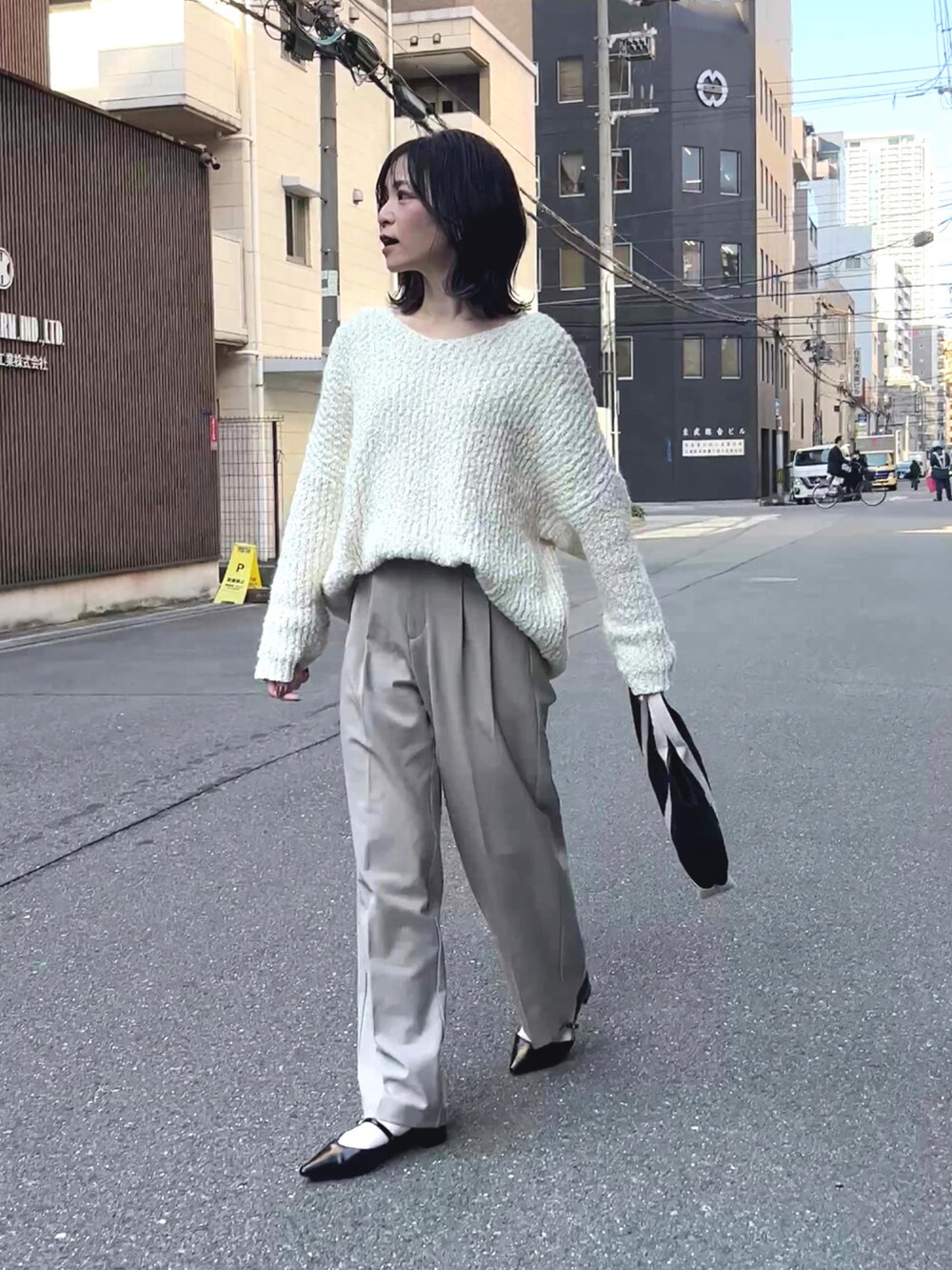 ブラック系のトートバッグ、ホワイト系のニット/セーター、ベージュ系のスラックスを着用したレディースの冬コーディネートの3枚目の写真