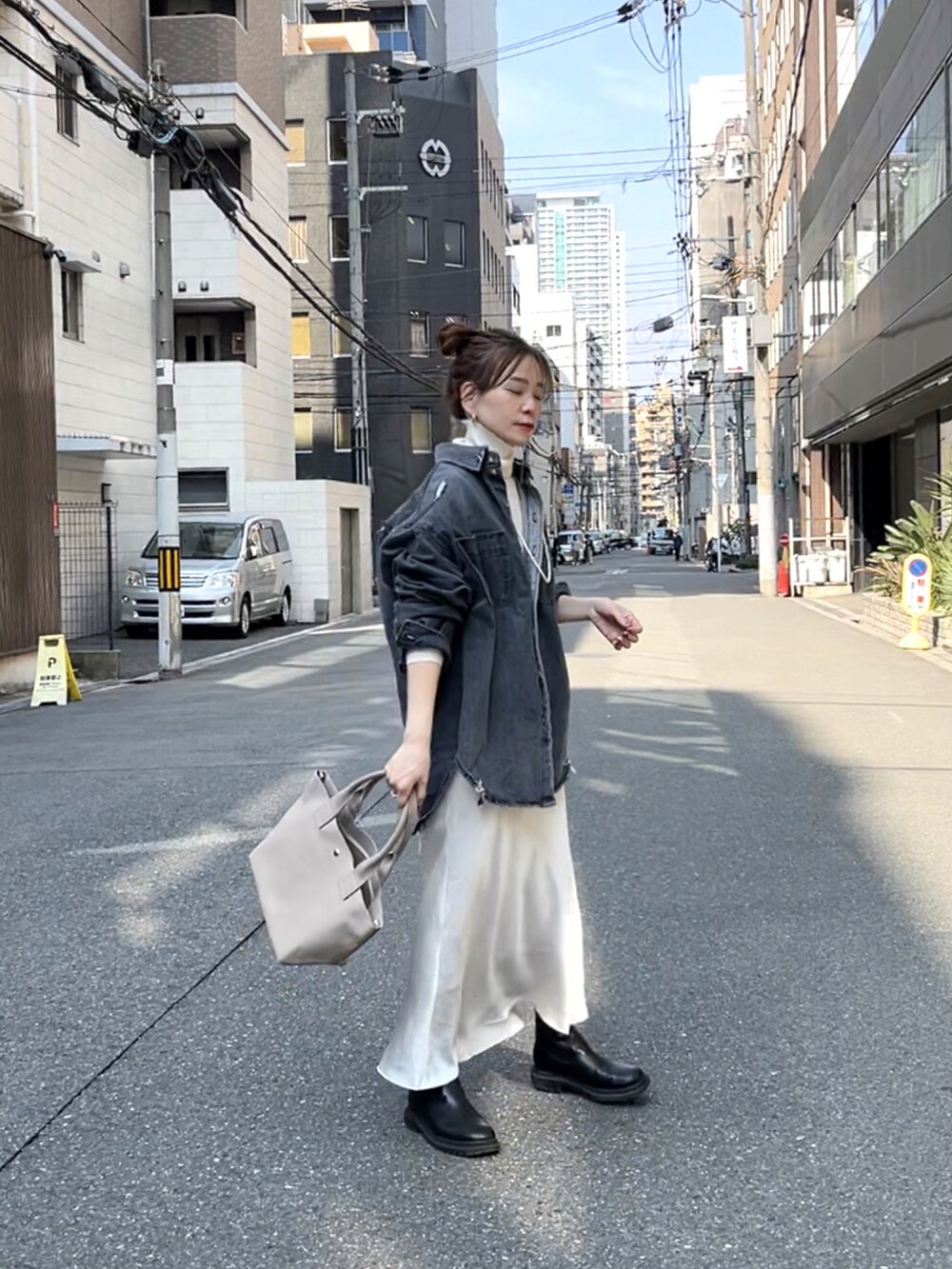 グレー系のトートバッグ、ブラック系のデニムジャケット、ホワイト系のスカートを着用したレディースの春コーディネートの5枚目の写真