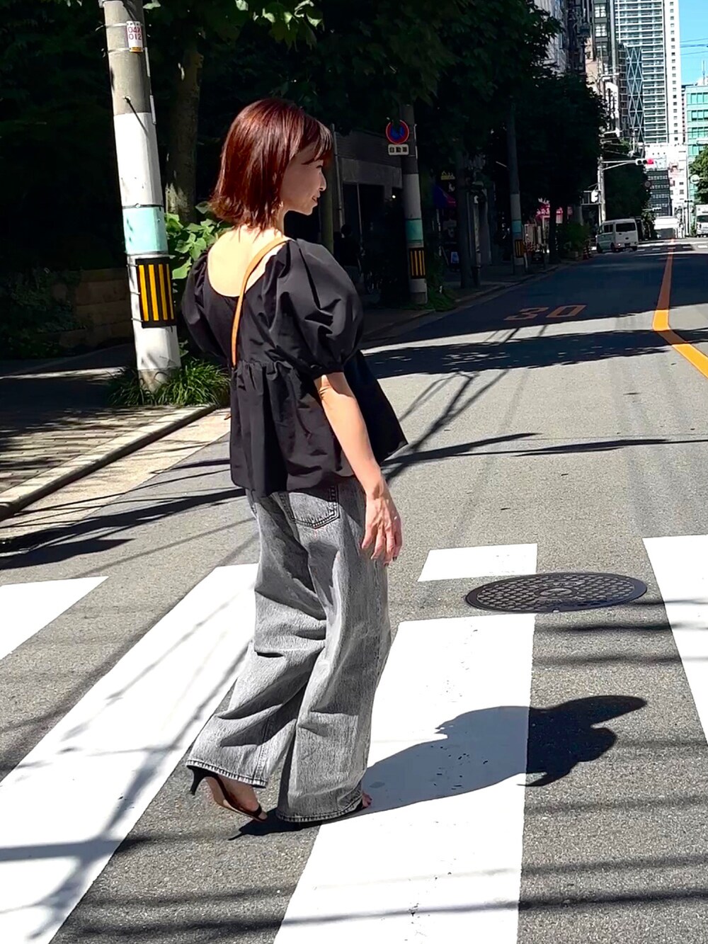 ブラック系のトップス、グレー系のデニムパンツ、ブラウン系のショルダーバッグを着用したレディースの夏コーディネートの3枚目の写真