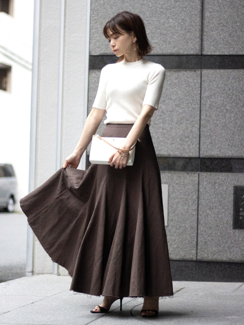 ホワイト系のハンドバッグ、ホワイト系のニット/セーター、ブラウン系のスカートを着用したレディースの夏コーディネートの2枚目の写真