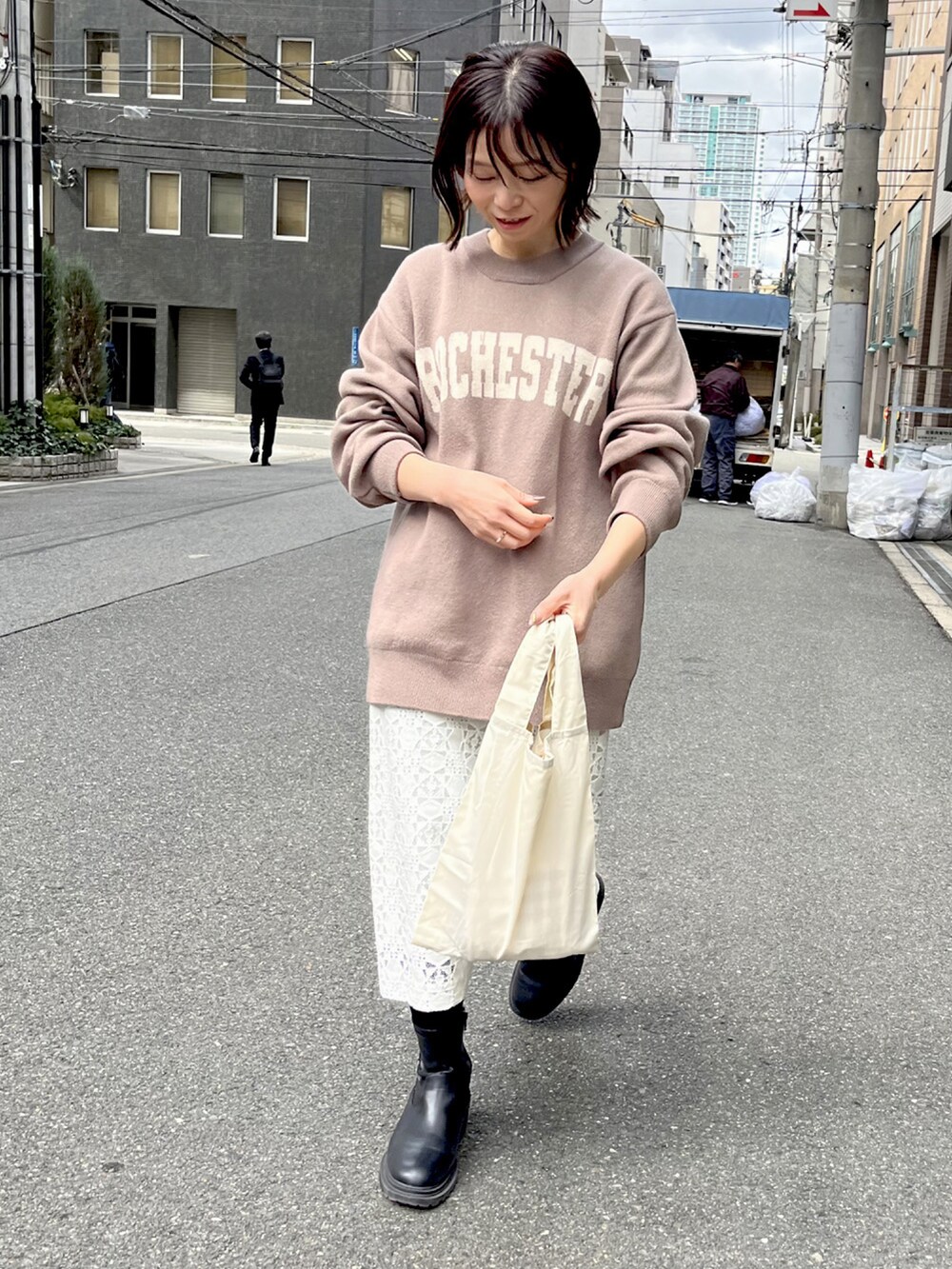 ベージュ系のニット/セーター、ベージュ系のエコバッグ/サブバッグ、ホワイト系のスカートを着用したレディースの春コーディネートの2枚目の写真