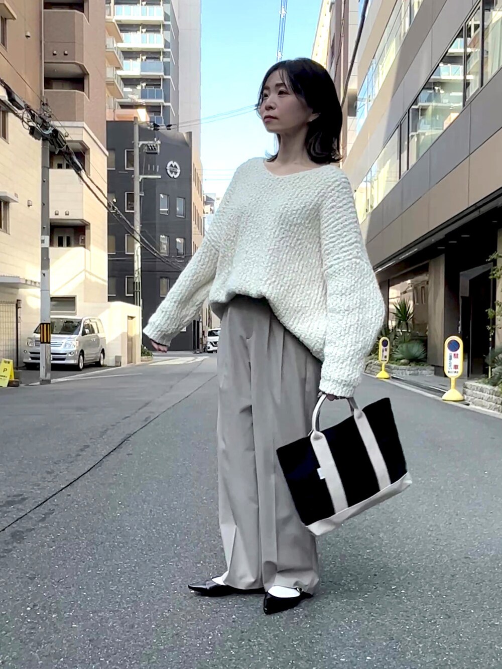 ブラック系のトートバッグ、ホワイト系のニット/セーター、ベージュ系のスラックスを着用したレディースの冬コーディネートの4枚目の写真