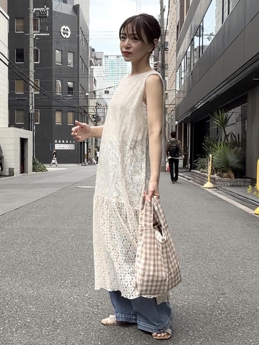 ベージュ系のワンピース、ベージュ系のエコバッグ/サブバッグ、ブルー系のデニムパンツを着用したレディースの夏コーディネートの2枚目の写真