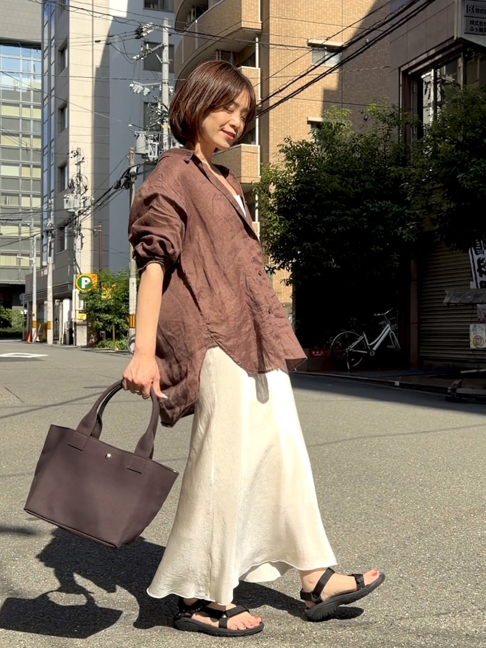 グレー系のトートバッグ、ブラウン系のシャツ/ブラウス、ブラック系のサンダルを着用したレディースの春コーディネートの2枚目の写真