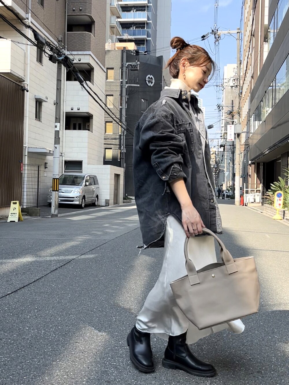 グレー系のトートバッグ、ブラック系のデニムジャケット、ホワイト系のスカートを着用したレディースの春コーディネートの3枚目の写真