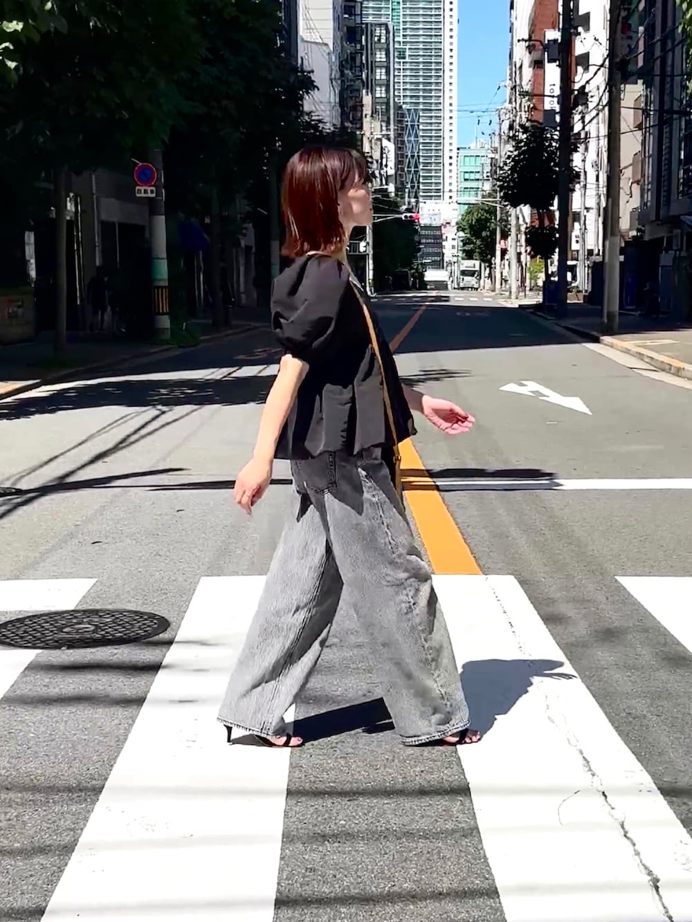 ブラック系のトップス、グレー系のデニムパンツ、ブラウン系のショルダーバッグを着用したレディースの夏コーディネートの2枚目の写真