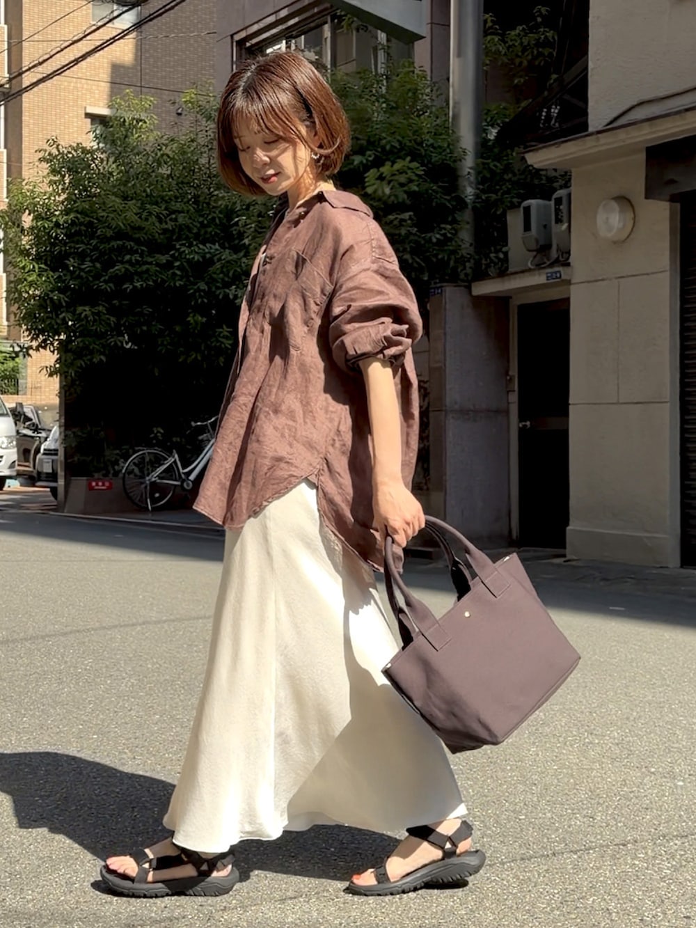 グレー系のトートバッグ、ブラウン系のシャツ/ブラウス、ブラック系のサンダルを着用したレディースの春コーディネートの3枚目の写真