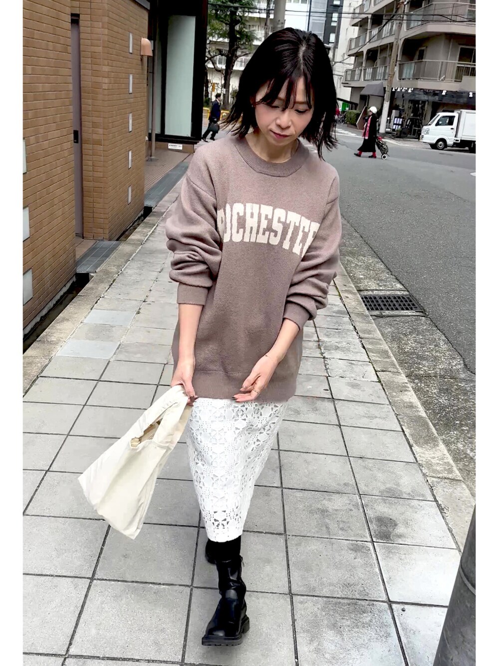 ベージュ系のニット/セーター、ベージュ系のエコバッグ/サブバッグ、ホワイト系のスカートを着用したレディースの春コーディネートの3枚目の写真