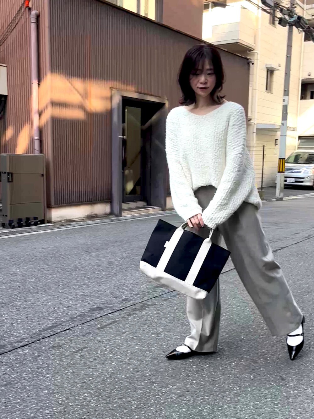 ブラック系のトートバッグ、ホワイト系のニット/セーター、ベージュ系のスラックスを着用したレディースの冬コーディネートの2枚目の写真