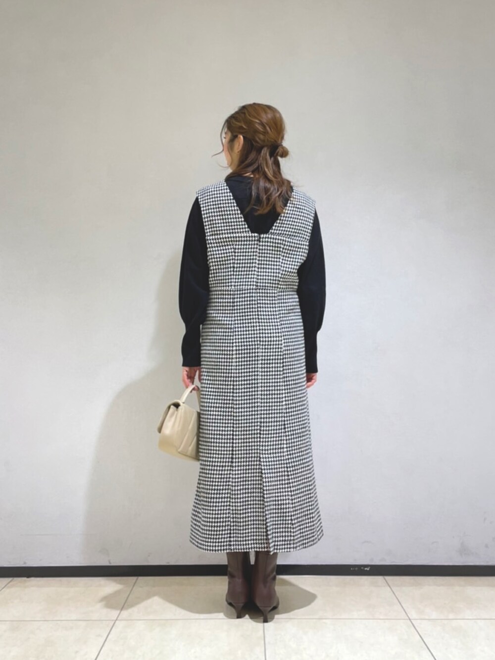 ホワイト系のジャンパースカート、ブラック系のニット/セーター、ベージュ系のショルダーバッグを着用したレディースの冬コーディネートの3枚目の写真