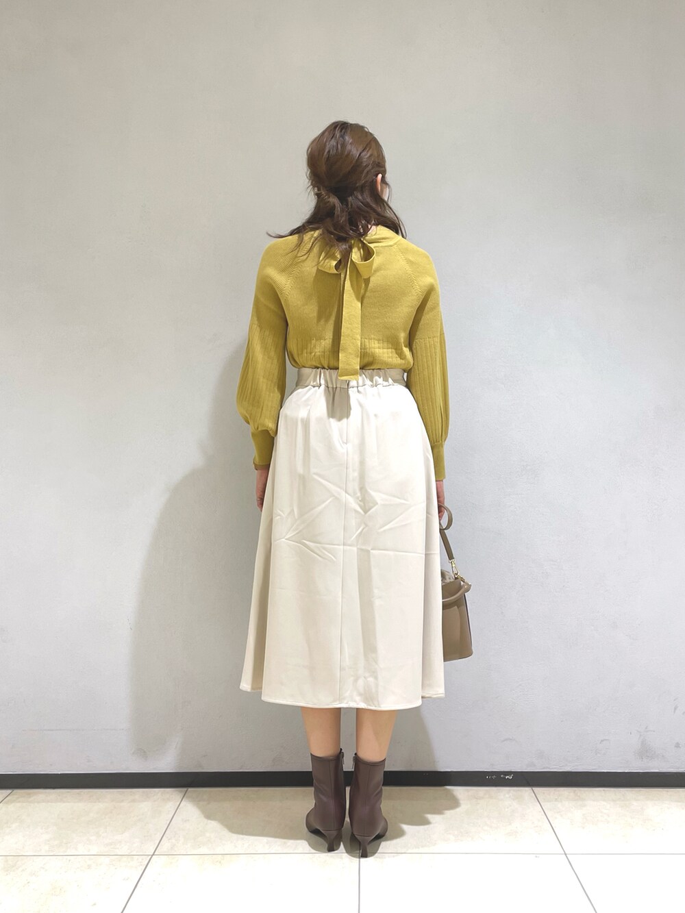 イエロー系のニット/セーター、イエロー系のショルダーバッグ、ベージュ系のスカートを着用したレディースの秋コーディネートの3枚目の写真