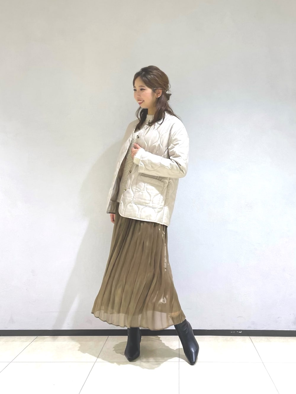 ベージュ系のノーカラーコート、ホワイト系のニット/セーター、グレー系のスカートを着用したレディースの秋コーディネートの2枚目の写真