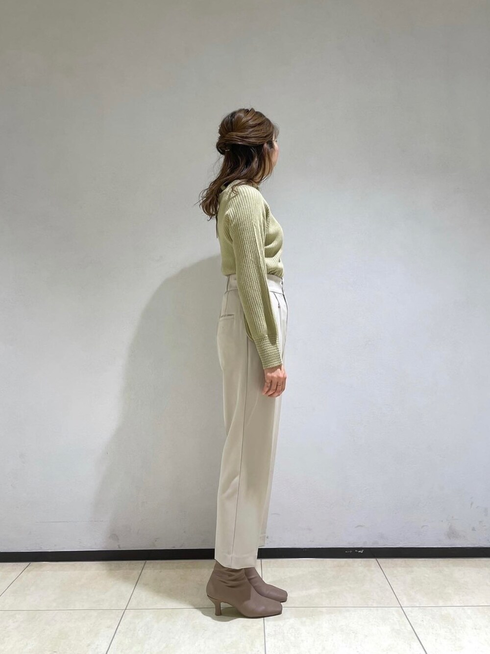 ブラック系のノーカラーコート、ベージュ系のその他パンツ、グリーン系のニット/セーターを着用したレディースの冬コーディネートの3枚目の写真