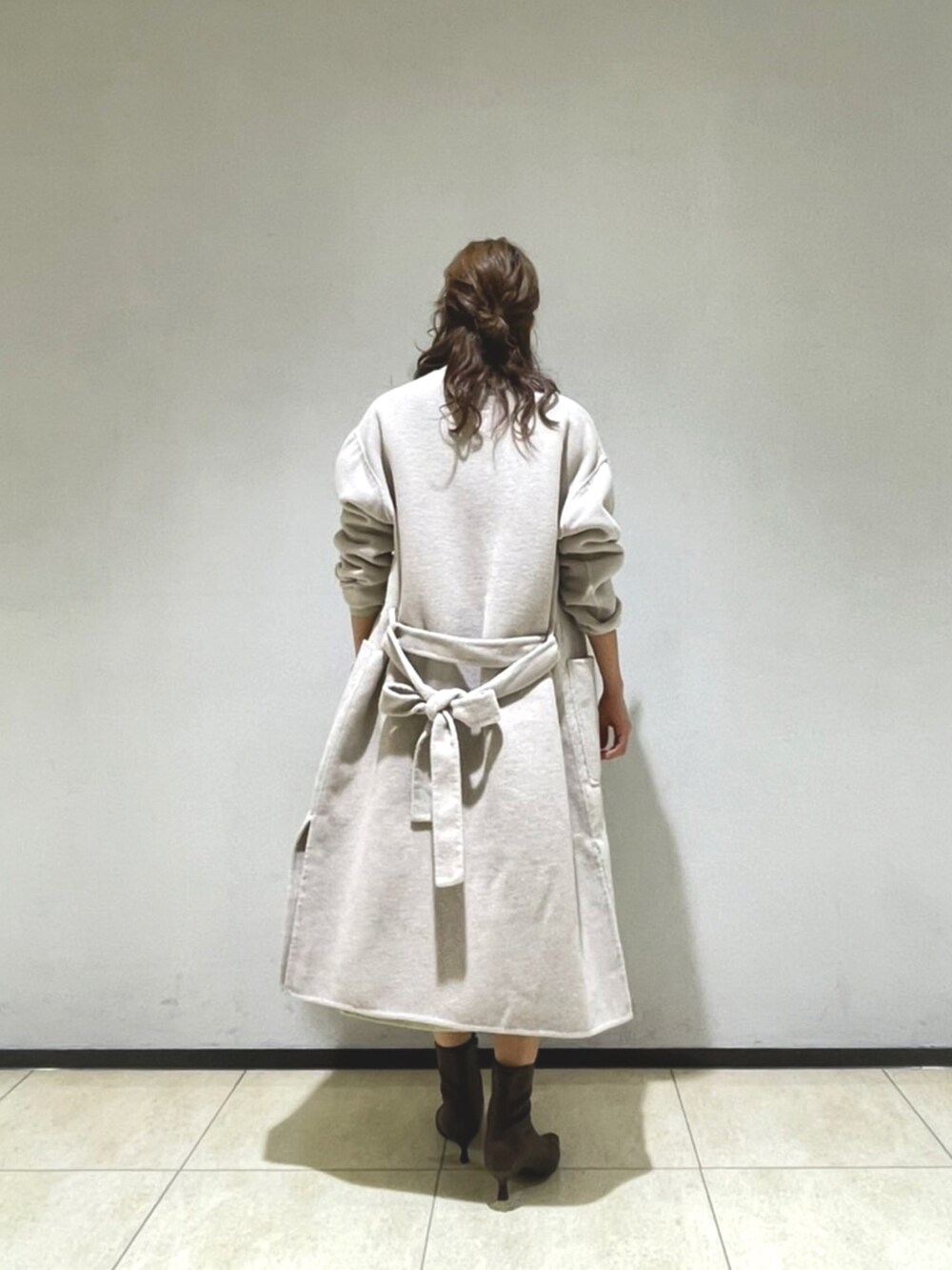 ベージュ系のノーカラーコート、グリーン系のワンピース、ブラウン系のブーツを着用したレディースの秋コーディネートの3枚目の写真