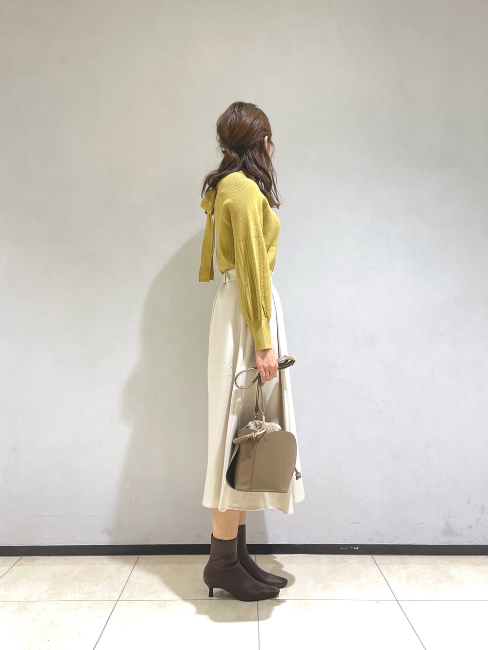 イエロー系のニット/セーター、イエロー系のショルダーバッグ、ベージュ系のスカートを着用したレディースの秋コーディネートの2枚目の写真