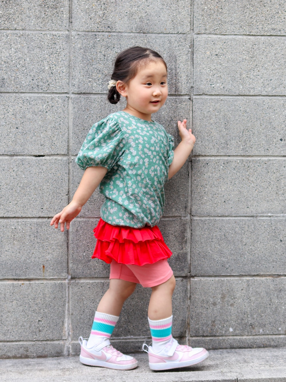 グリーン系のトップス、レッド系のスカート、ホワイト系のスニーカーを着用したキッズの夏コーディネートの2枚目の写真