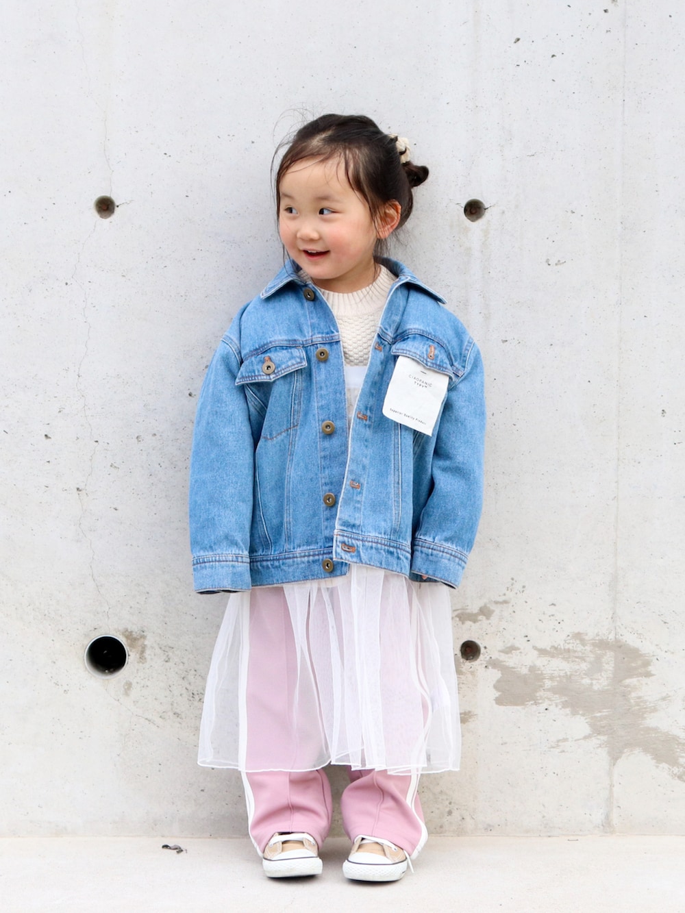 ブルー系のデニムジャケット、ホワイト系のニット/セーター、ホワイト系のワンピースを着用したキッズの冬コーディネートの3枚目の写真