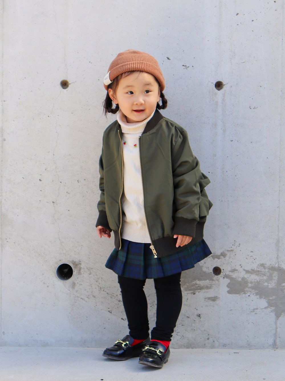 グリーン系のMA-1、ホワイト系のニット/セーター、グリーン系のスカートを着用したキッズの秋コーディネートの2枚目の写真