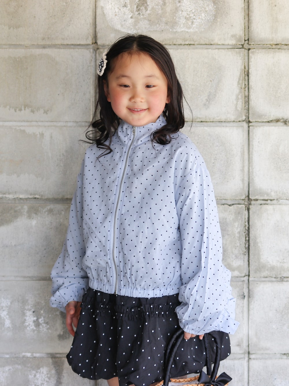 ブルー系のナイロンジャケット、ブラック系のスカート、ブラック系のかごバッグを着用したキッズの春コーディネートの3枚目の写真